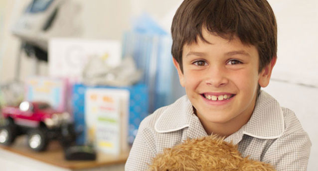 cute little boy with gaps in his teeth smiling and holding a teddy bear