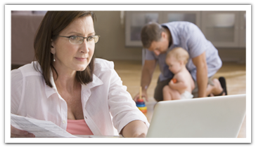 a woman reviewing information on her laptop while dad and baby play in the background