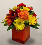 a square orange vase with an arrangement of yellow, orange and red flowers